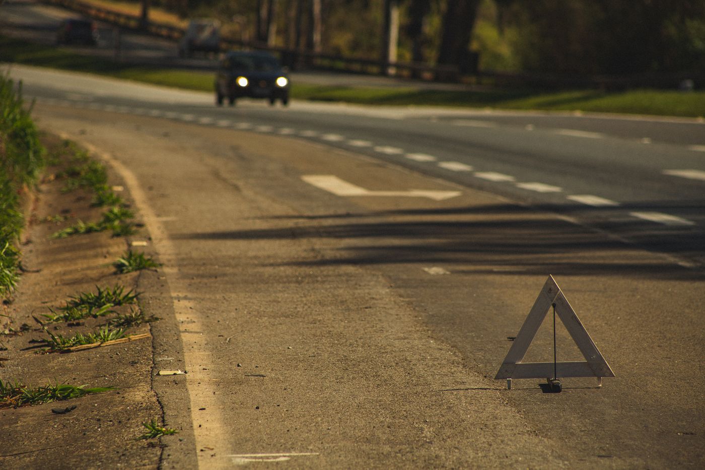 Triangolo d’emergenza posato sul ciglio della strada, con un’automobile che arriva coi fari accesi